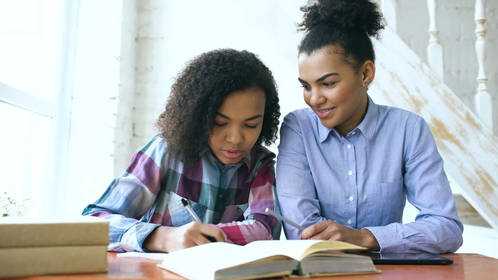 Teen studying with an adult at a home table, focusing on learning and education.